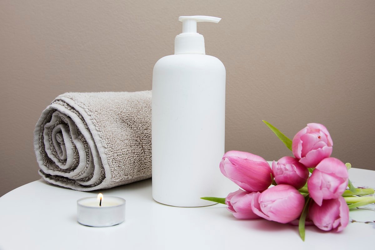 A curated in-room amenity set — rolled towel, signature bath dispenser, candle, and fresh flowers